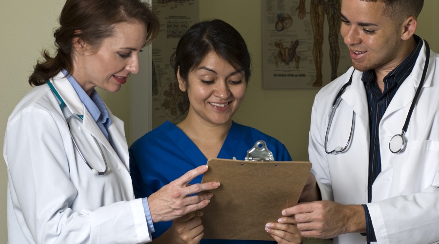 Two doctors and a nurse smiling at the information they are reviewing on a clipboard.